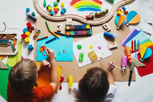 heads of two children making art with lots of colorful art supplies