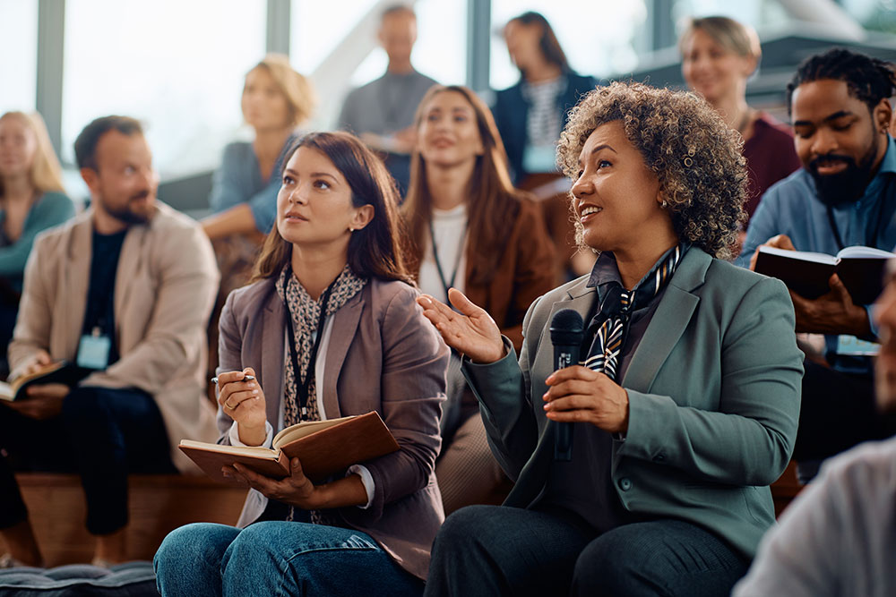  A gathering of people in a lecture hall, seated and listening intently to a presentation and taking notes.