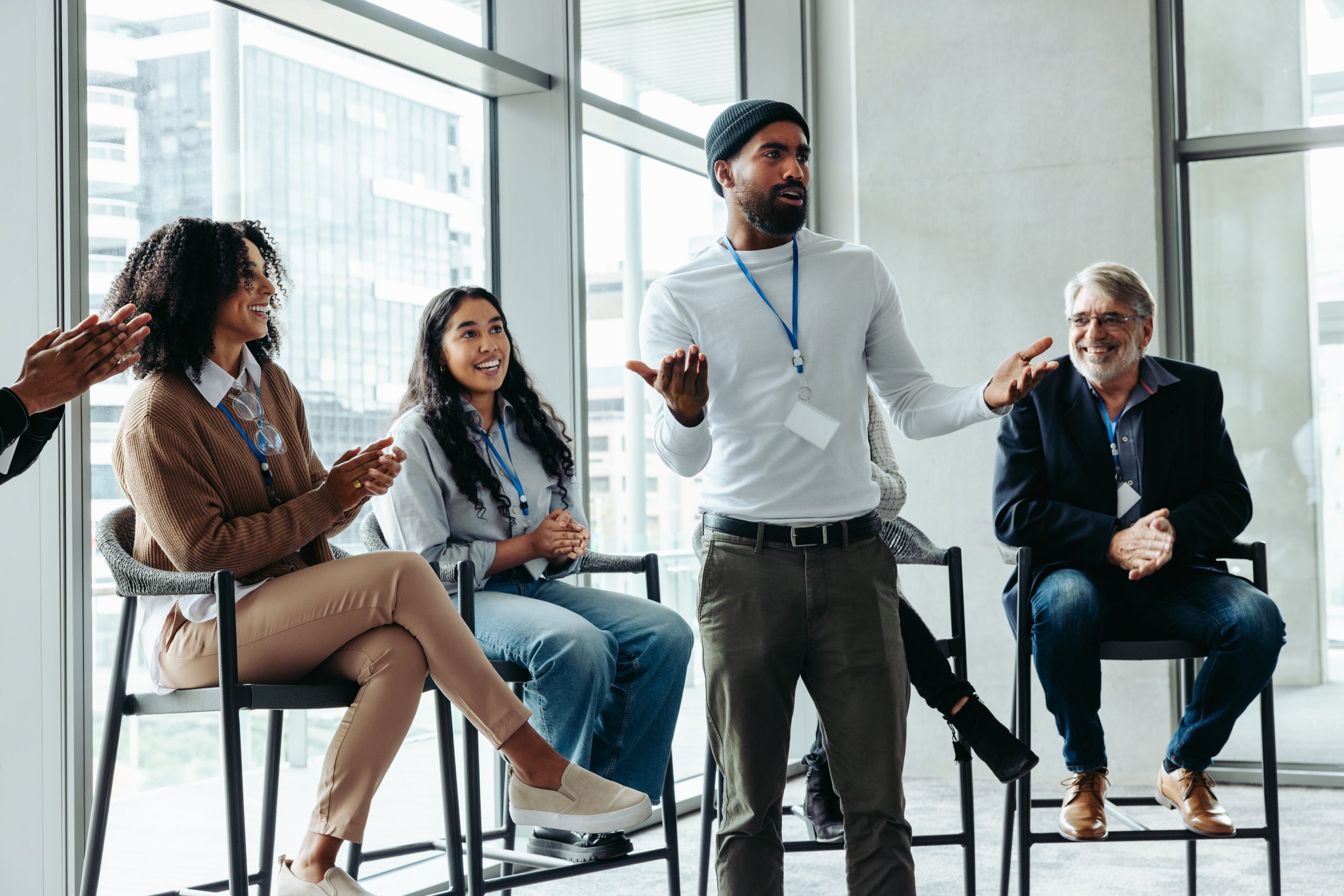 Diverse group of professionals participating in an active meeting, with one individual speaking while others listen, smile, and applaud.