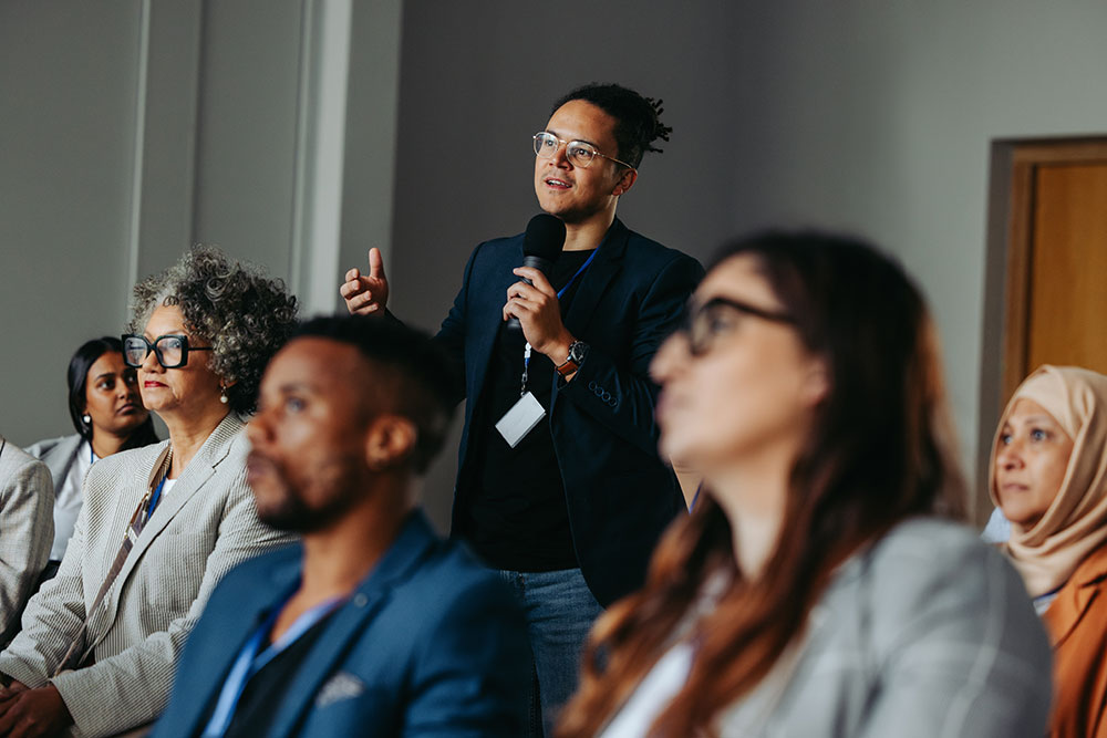 A speaker delivers a presentation to an attentive group, highlighting key points with visual aids in a professional setting.